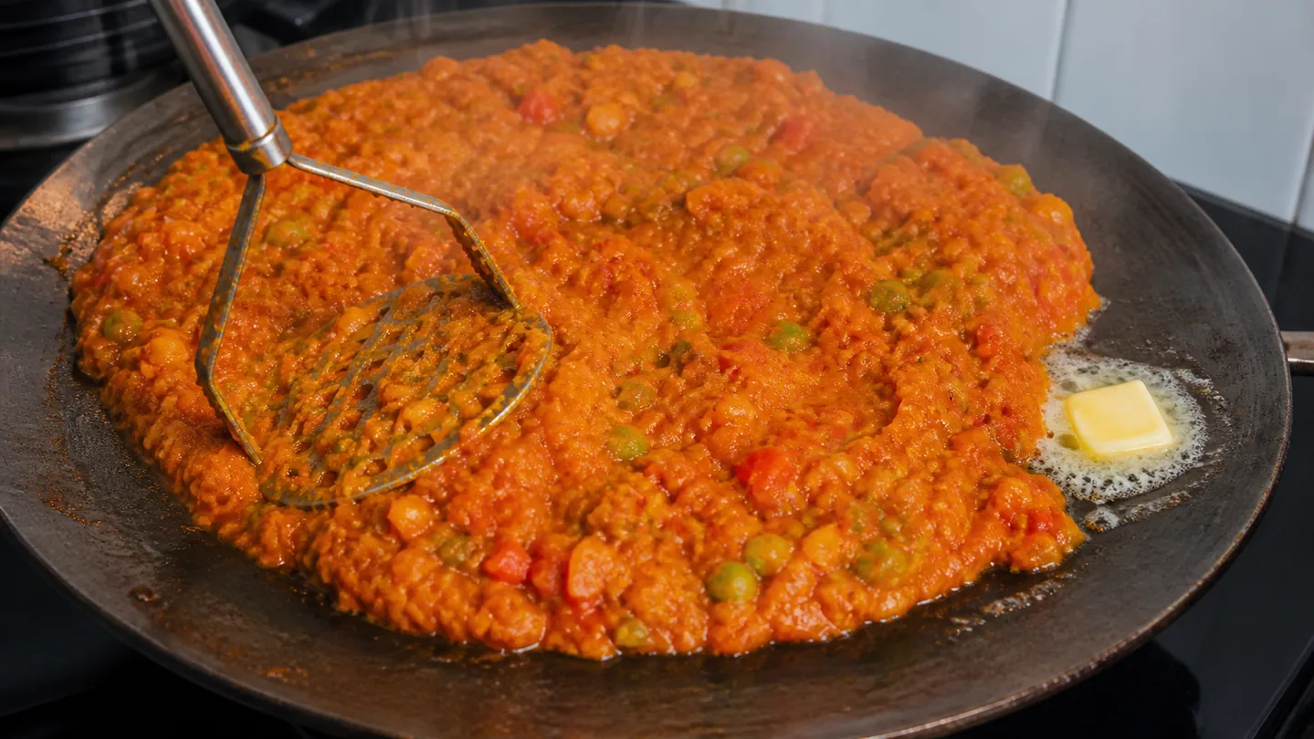 Zeleninová směs Pav Bhaji mačkaná šťouchadlem na široké pánvi
